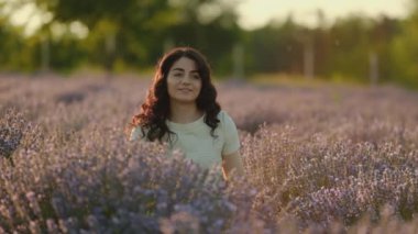 Genç, güzel, esmer bir kadın yazın gün batımında açan lavanta tarlasında yürüyor..