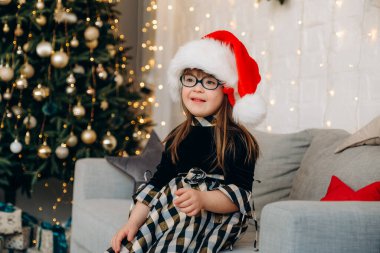 Down sendromlu küçük bir kız kanepeye oturmuş Noel Baba şapkası takıyor ve Noel hediyelerini bekliyor. Down sendromlu bir çocuğu büyütmekte güçlük çekiyorlar..