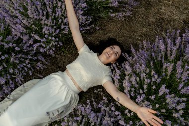 Güzel bir esmer lavanta tarlasında yatıyor. Yazın kırsal bölgelerdeki çiçek açan tarlalara seyahat et..