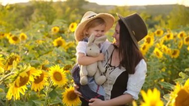 Küçük kız ve annesi yazın açan ayçiçeği tarlasında yürüyorlar. Mutlu çocuklar yetiştirmek. Anne ve kızı ayçiçeği tarlasında yürüyor..