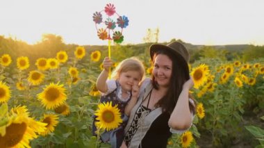 Küçük kız ve annesi yazın açan ayçiçeği tarlasında yürüyorlar. Mutlu çocuklar yetiştirmek. Anne ve kızı ayçiçeği tarlasında yürüyor..