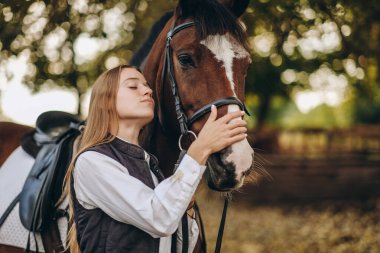 Genç bir dişi binici atının yanında duruyor ve bir yarışa hazırlanıyor. Atlama eğitimini göster. Atları severim..