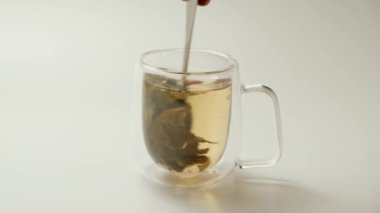Bir adam çay kaşığıyla beyaz arka planda çay karıştırır. Sağlıklı yeşil çay yapmak.