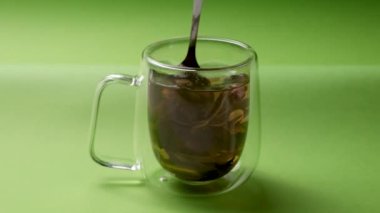 Bir adam yeşil arka planda çay kaşığıyla çayı karıştırır. Sağlıklı yeşil çay yapmak.