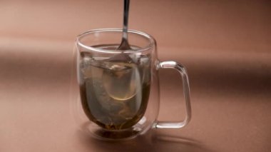 Kahverengi arka planda çay kaşığıyla çay karıştıran bir adam. Sağlıklı yeşil çay yapmak.