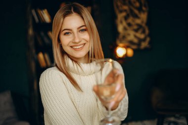 A young beautiful woman with a glass of champagne smiles and sits in the house on the eve of Christmas. Celebrating Christmas. clipart