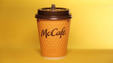 Masanın üzerinde sarı bir McCoffee bardağı duruyor. Bardağın aydınlatma düzgünce değişiyor. Düzenleyici video.
