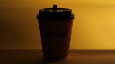 Masanın üzerinde sarı bir McCoffee bardağı duruyor. Bardağın aydınlatma düzgünce değişiyor. Düzenleyici video.