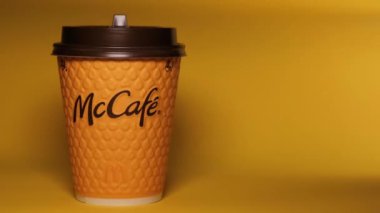 Masanın üzerinde sarı bir McCoffee bardağı duruyor. Bardağın aydınlatma düzgünce değişiyor. Düzenleyici video.