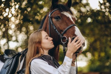 Genç bir dişi binici atının yanında duruyor ve bir yarışa hazırlanıyor. Atlama eğitimini göster. Atları severim..