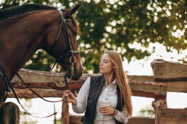Genç bir dişi binici atının yanında duruyor ve bir yarışa hazırlanıyor. Atlama eğitimini göster. Atları severim..