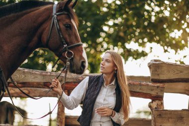 Genç bir dişi binici atının yanında duruyor ve bir yarışa hazırlanıyor. Atlama eğitimini göster. Atları severim..