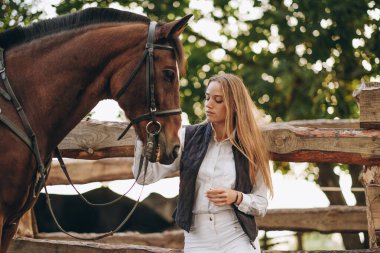 Genç bir dişi binici atının yanında duruyor ve bir yarışa hazırlanıyor. Atlama eğitimini göster. Atları severim..