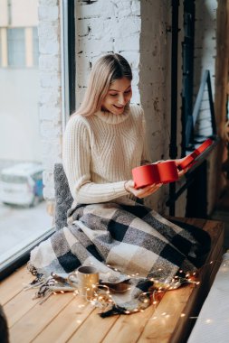 Young beautiful blonde opens a gift for Valentine's Day. A woman opens a red box in the form of a heart with a gift.