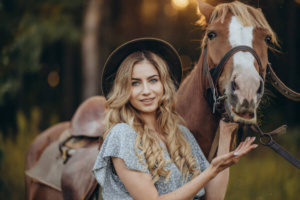 A young beautiful woman walks with her horse in the forest in early autumn. Walking with a horse in the forest.