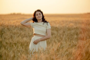 Genç bir esmer yazın günbatımında buğday tarlalarında yürür. Organik buğday ve arpa yetiştiriyor..
