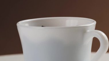 Aromatik taze kavrulmuş kahve çekirdekleri kahverengi arka planda beyaz bir kahve bardağına dökülüyor..