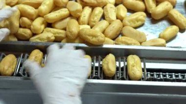 Üretim hattında bir sürü tatlı krema pişiriyor. tatlı yemek konsepti. Yeni pişmiş, çıtır çıtır, dikdörtgen ekler. Geleneksel Fransız ekleriymiş. Kalite 4K video yakalama.