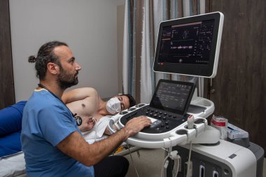 İstanbul, Türkiye - 20 Eylül 2022; Doktor ultrason cihazı kullanarak hastayı muayene ediyor. Ultrason sensörünü hasta kabinesinden geçiriyor. Tanısal muayene.