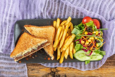 Çedar peynirli kulüp tostu. Eritilmiş peynirli tost sandviçi ve kızarmış et. Kızarmış et, tost ve salata ile servis edilir..