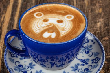 Ahşap masada mavi porselen bir fincan sıcak latte sanat kahvesi. Güzel Latte sanatıyla birlikte bir fincan kahve. Kahve dükkanında menü, dinlenme tatili. Yüksek kaliteli fotoğrafçılık.