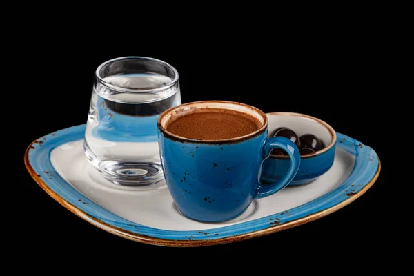 Turkish coffee in a blue cup, chocolate on a porcelain serving tray, water and a coffee cup. Isolated on black background. Menu in coffee shop, relaxing time holidays. High quality photography.