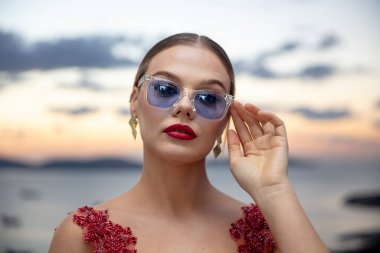 Gün batımında renkli gözlük takan güzel bir kadın model. Açık havada, makyajlı ve gözlüklü çekici sarışın bir kadının romantik portresi. İstanbul takımadaları (Prenses Adaları) ufuk çizgisi.