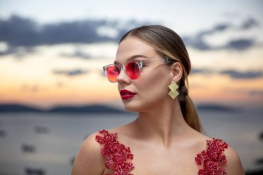 Gün batımında renkli gözlük takan güzel bir kadın model. Açık havada, makyajlı ve gözlüklü çekici sarışın bir kadının romantik portresi. İstanbul takımadaları (Prenses Adaları) ufuk çizgisi.
