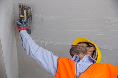 İnşaattaki bir sıva ustası tulum ve şapka giyer. Oyun hamuru bıçağıyla bir duvara macun yapıştırıyor. Onarım ve inşaat konsepti.