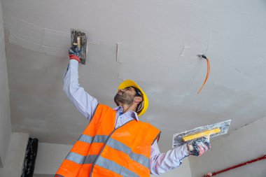 İnşaattaki bir sıva ustası tulum ve şapka giyer. Oyun hamuru bıçağıyla bir duvara macun yapıştırıyor. Onarım ve inşaat konsepti.