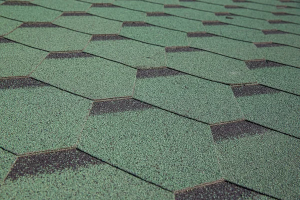Roofing made of green soft bitumen tiles on a hipped roof of a house. Close up view of Asphalt Roofing green Tile Background. Green tiles on the roof of the house. Roof Shingles, Roofing Repair.