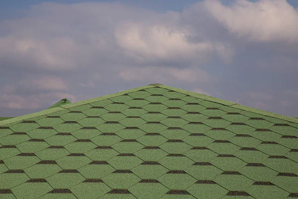 Roofing made of green soft bitumen tiles on a hipped roof of a house. Close up view of Asphalt Roofing green Tile Background. Green tiles on the roof of the house. Roof Shingles, Roofing Repair.