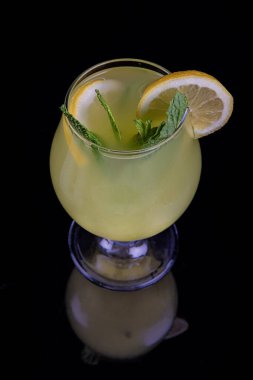 A glass of fresh lemonade, lemon juice. Cocktail with lemon slices and lemon slice on a black background. Copy space.