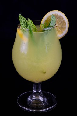 A glass of fresh lemonade, lemon juice. Cocktail with lemon slices and lemon slice on a black background. Copy space.
