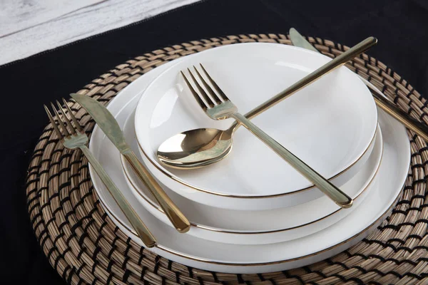 Plates and utensils, Plate, Bowl and golden cutlery against dining table background, side view. Modern craft ceramic tableware.