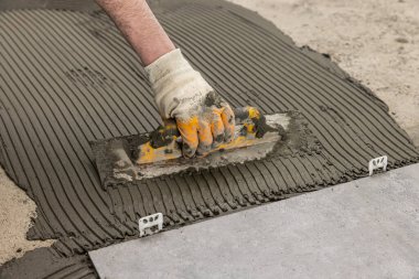 industrial ceramic builder worker installing floor tile at repair renovation work - Handyman installing ceramic tiles - A special cement mass to fill gaps between the laid ceramics.