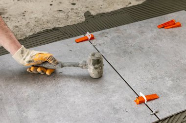 industrial ceramic builder worker installing floor tile at repair renovation work - Handyman installing ceramic tiles - A special cement mass to fill gaps between the laid ceramics.