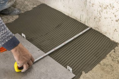 industrial ceramic builder worker installing floor tile at repair renovation work - Handyman installing ceramic tiles - A special cement mass to fill gaps between the laid ceramics.