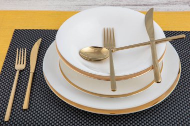 Tabaklar ve kaplar, tabak, kase ve yemek masasında altın çatal bıçak takımı, yan görüş. Modern zanaat seramik sofra takımı, yemek masasında çatal bıçak takımı..