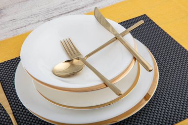 Tabaklar ve kaplar, tabak, kase ve yemek masasında altın çatal bıçak takımı, yan görüş. Modern zanaat seramik sofra takımı, yemek masasında çatal bıçak takımı..