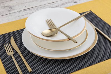 Tabaklar ve kaplar, tabak, kase ve yemek masasında altın çatal bıçak takımı, yan görüş. Modern zanaat seramik sofra takımı, yemek masasında çatal bıçak takımı..