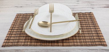 Tabak, kap kase, tabak ve altın çatal bıçak seti hasır Amerikan yemeği masasında servis ediliyor. Modern zanaat seramik çatal bıçak takımı yemek masasında..