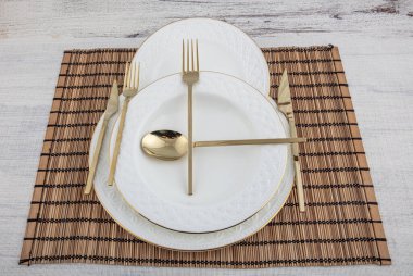 Tabak, kap kase, tabak ve altın çatal bıçak seti hasır Amerikan yemeği masasında servis ediliyor. Modern zanaat seramik çatal bıçak takımı yemek masasında..