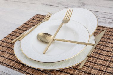 Tabak, kap kase, tabak ve altın çatal bıçak seti hasır Amerikan yemeği masasında servis ediliyor. Modern zanaat seramik çatal bıçak takımı yemek masasında..