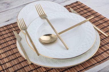 Tabak, kap kase, tabak ve altın çatal bıçak seti hasır Amerikan yemeği masasında servis ediliyor. Modern zanaat seramik çatal bıçak takımı yemek masasında..