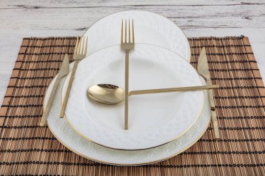 Tabak, kap kase, tabak ve altın çatal bıçak seti hasır Amerikan yemeği masasında servis ediliyor. Modern zanaat seramik çatal bıçak takımı yemek masasında..