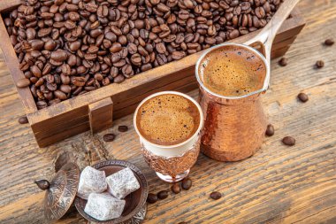 Bakır fincanda sade Türk kahvesi ve ahşap masaya saçılmış kahve çekirdekleri. Bakır bardakta geleneksel Türk kahvesi ve Türk lokumu, sıcak içecek konsepti.
