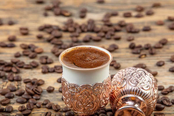 Black Turkish coffee in copper cup and roasted coffee beans scattered on wooden table. Traditional Turkish coffee in copper cup and Turkish delight, hot drink concept.