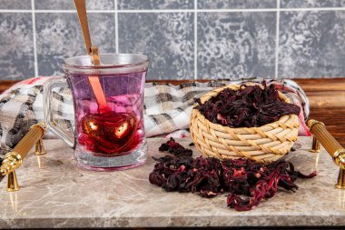 Beyaz ahşap masada, gül yapraklarıyla birlikte cam bardakta kırmızı amber çayı. Hibiscus çay arkaplanı.