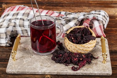 Beyaz ahşap masada, gül yapraklarıyla birlikte cam bardakta kırmızı amber çayı. Hibiscus çay arkaplanı.